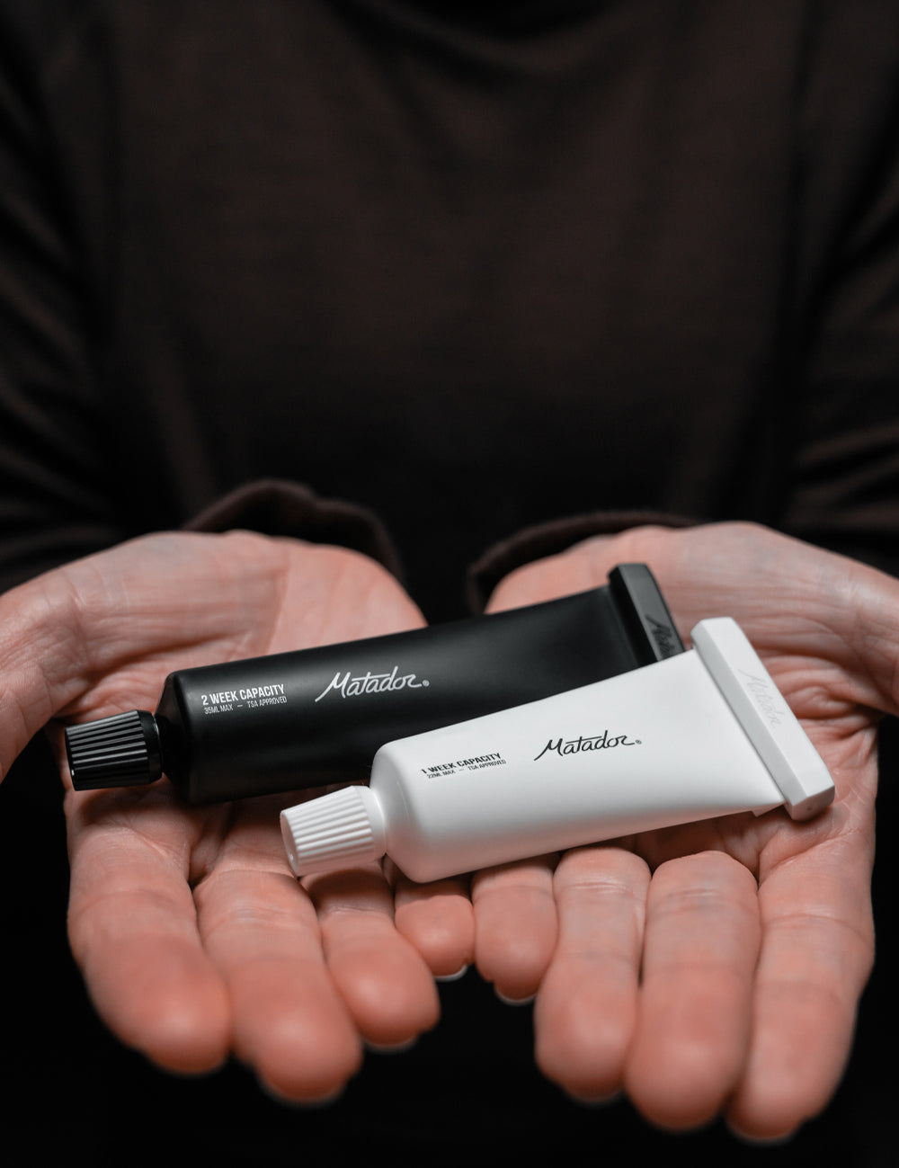 hands holding black and white toothpaste tubes