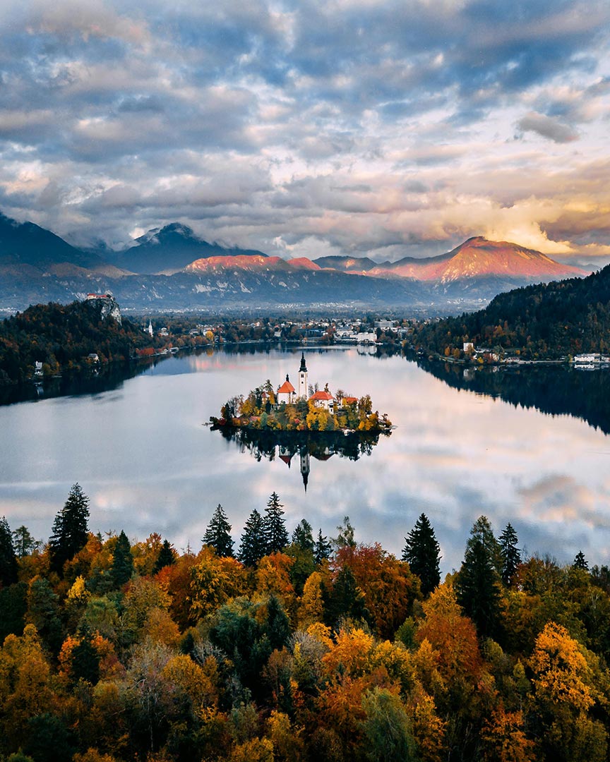 island with a church and mountains in the backgrouns with orange and green trees