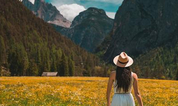 Woman in hat, standing in golden field with mountains in the background